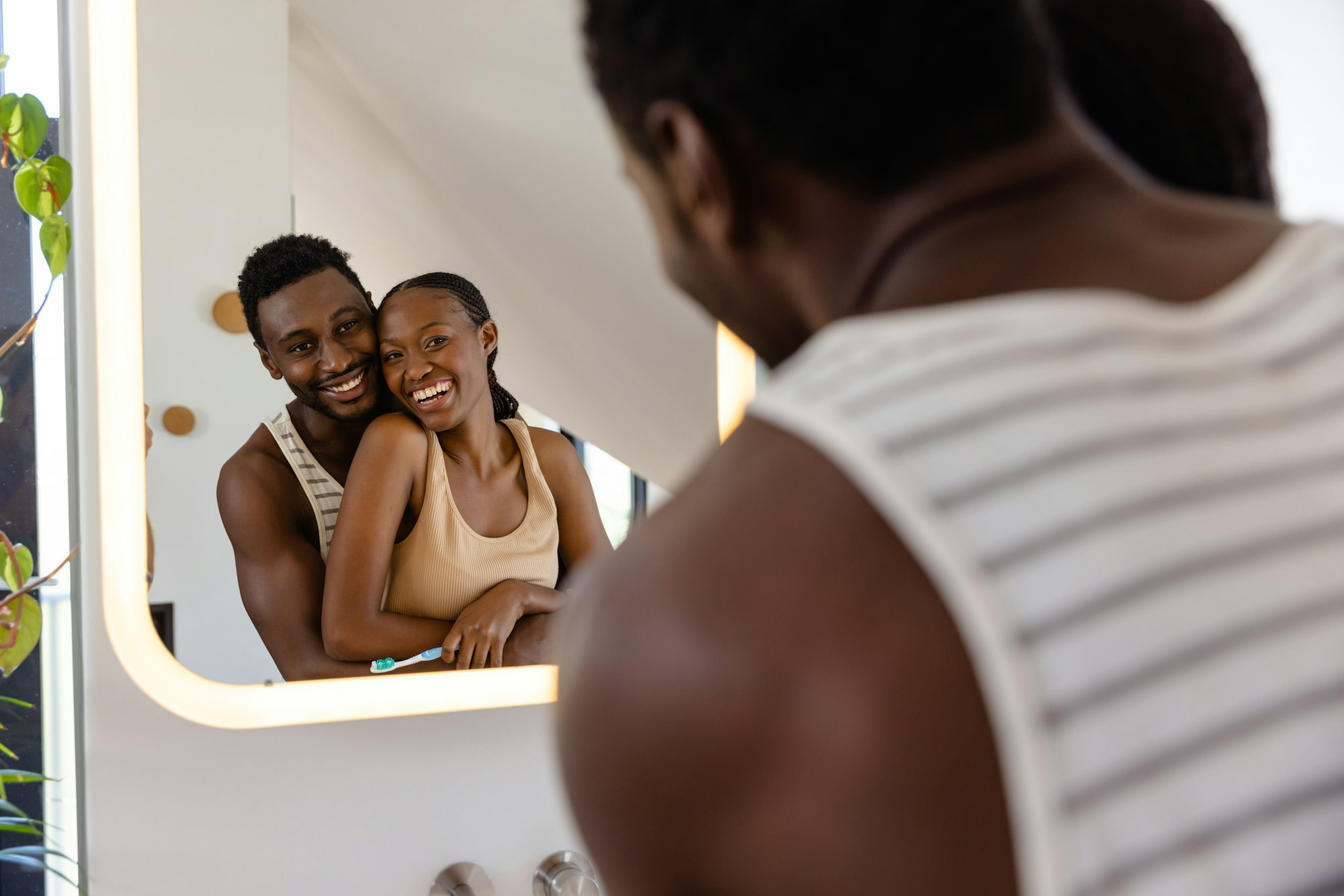 Happy african american couple brushing teeth and hugging in bathroom